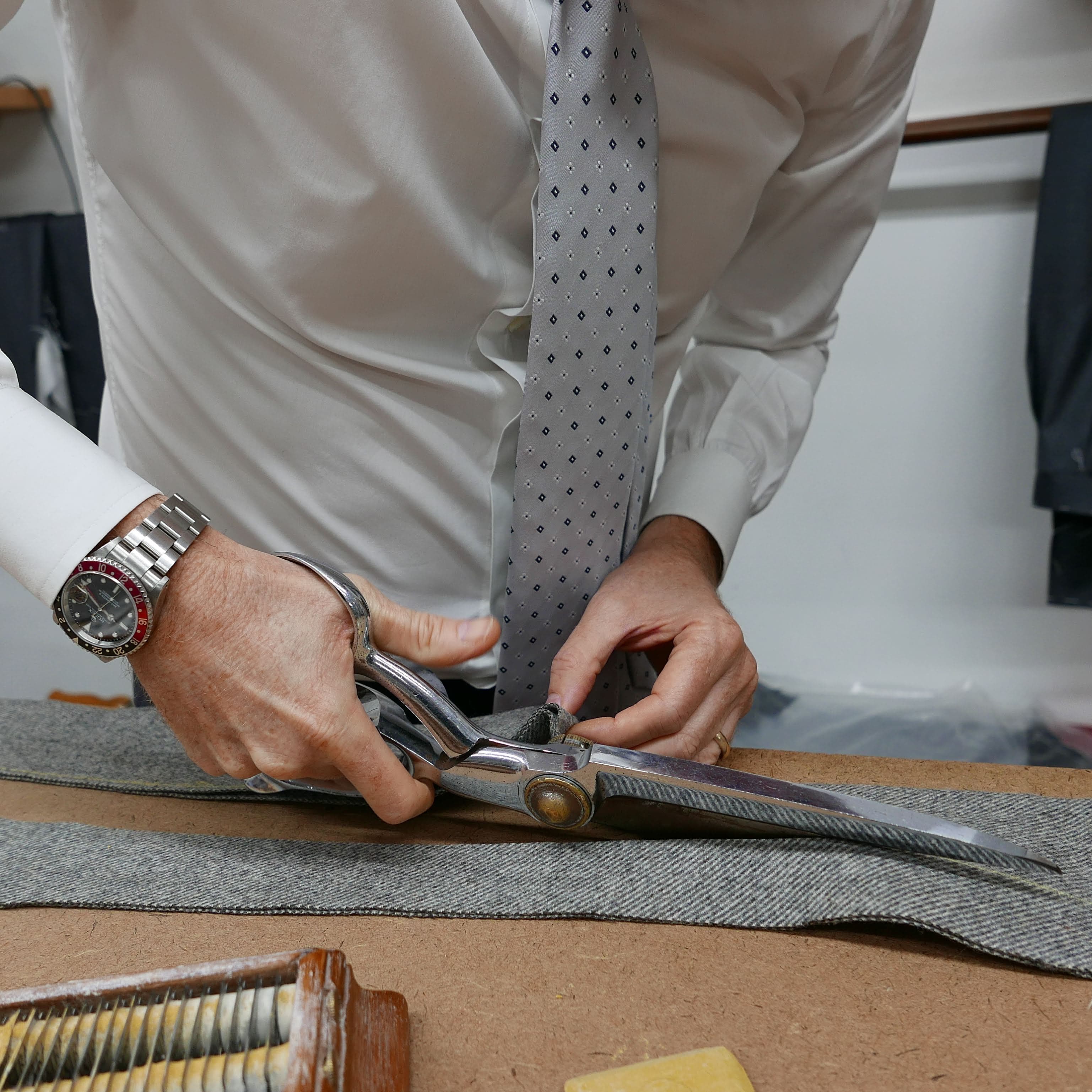 A tailor cuts a panel of grey cloth with large metal shears.