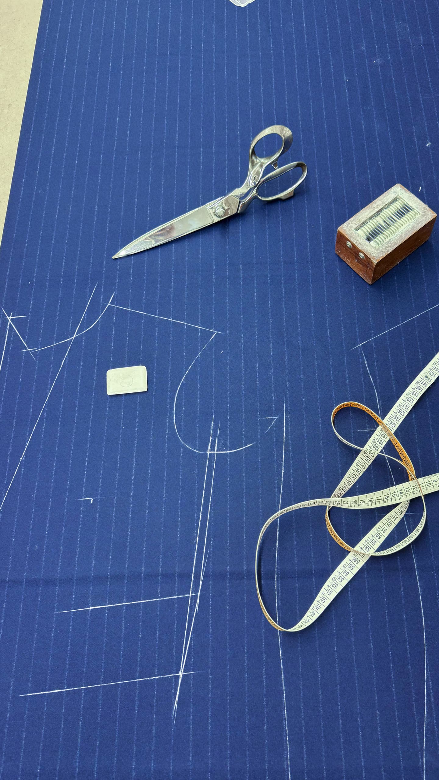 Tailor’s chalk lines, shears and a measuring tape on navy pinstripe cloth.