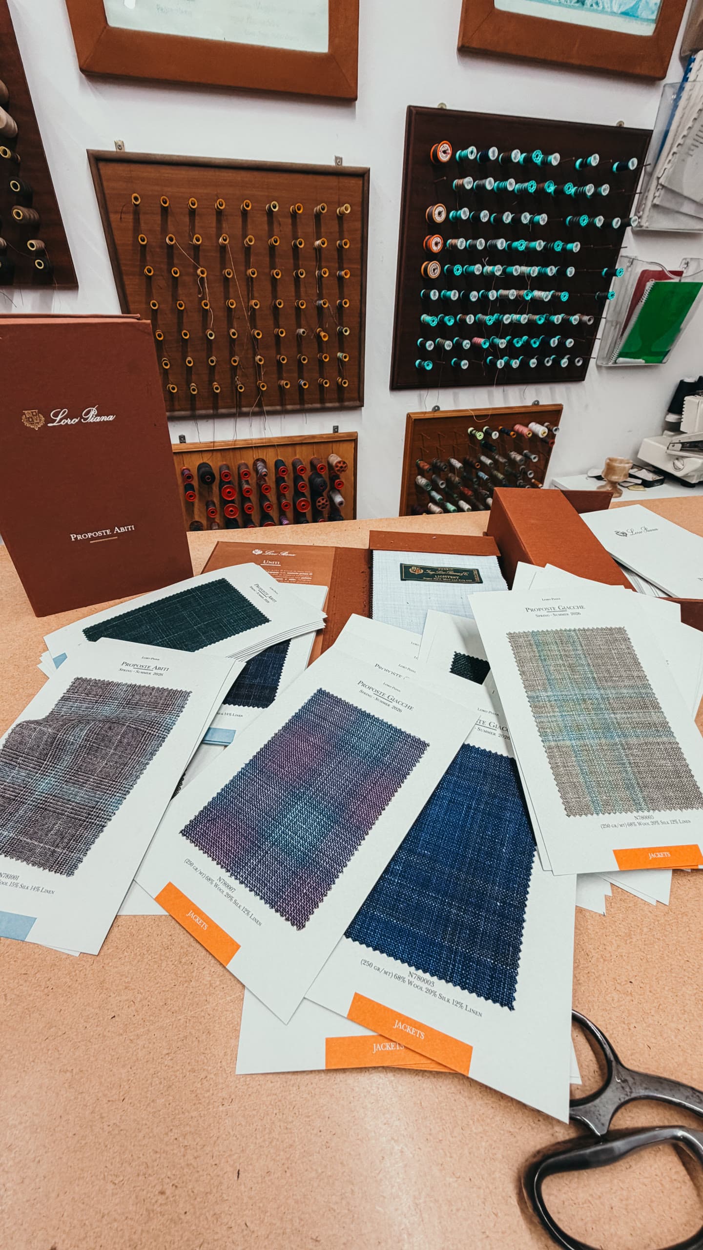 Fabric swatch cards, tailoring threads and shears arranged on an atelier worktable.