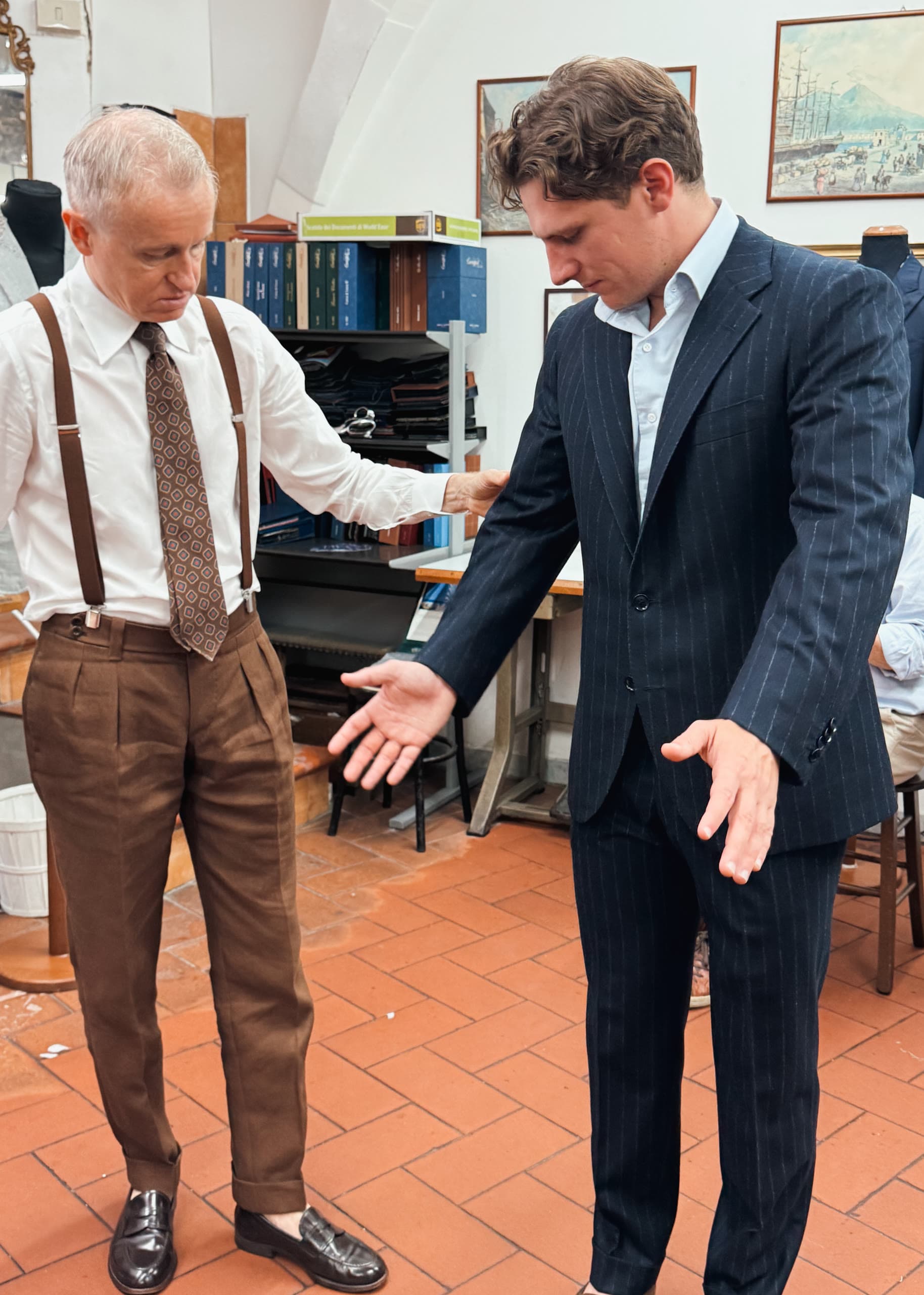 A tailor assesses a client wearing a finished navy pinstripe suit.
