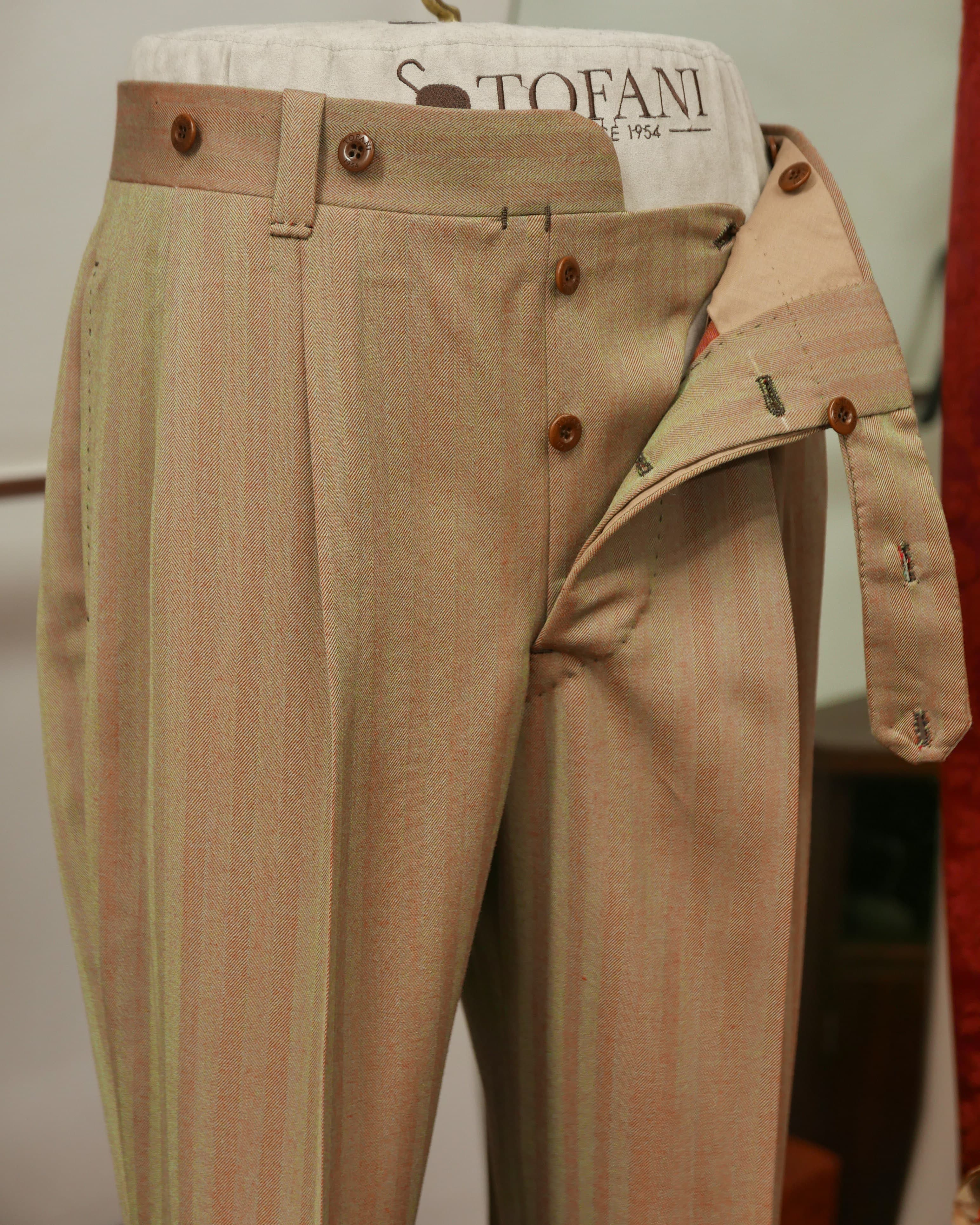Beige bespoke trousers on a form, open at the fly to show the rise, pleats and waistband.