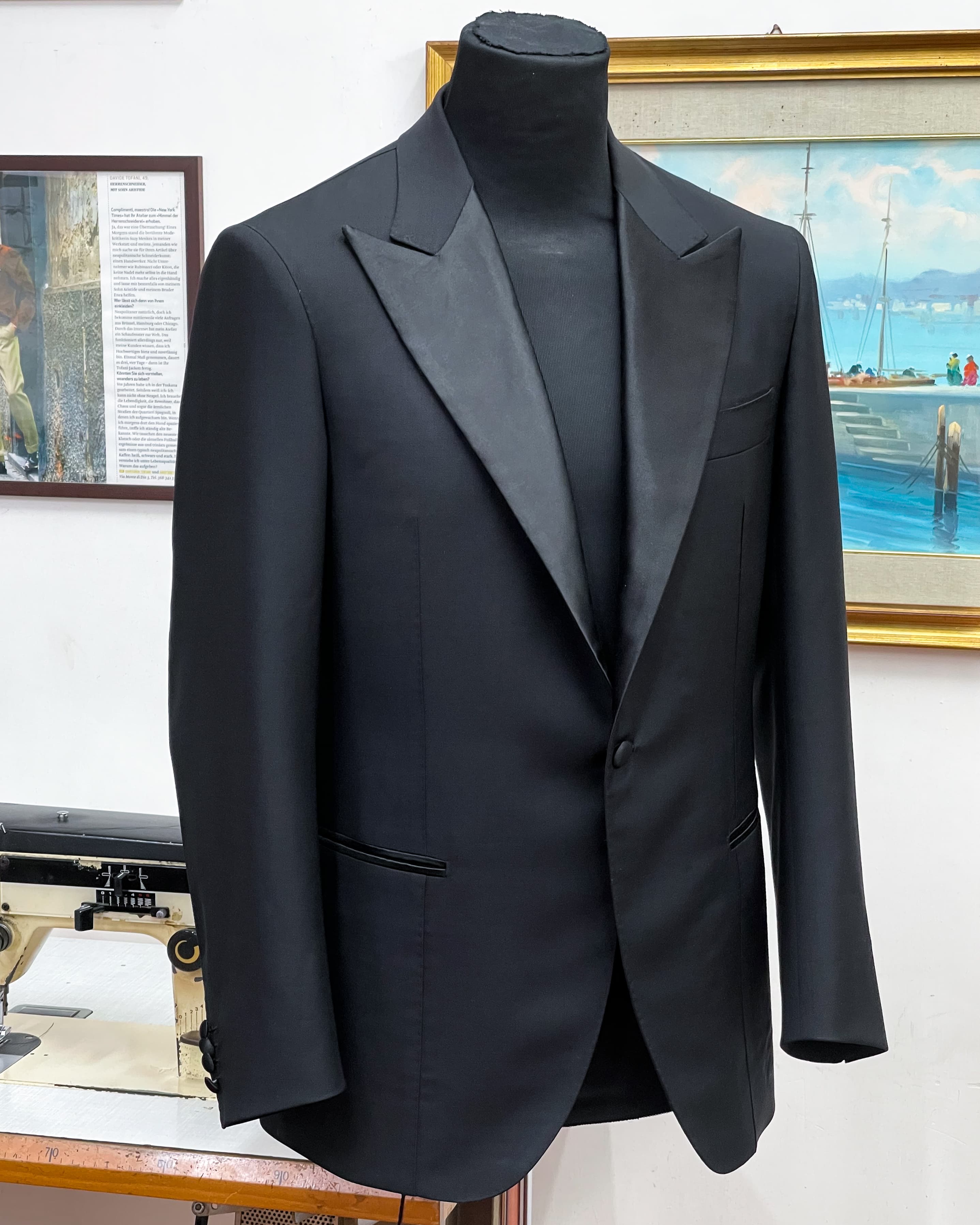 A black dinner jacket with satin peak lapels and a single button, displayed on a tailor’s form.