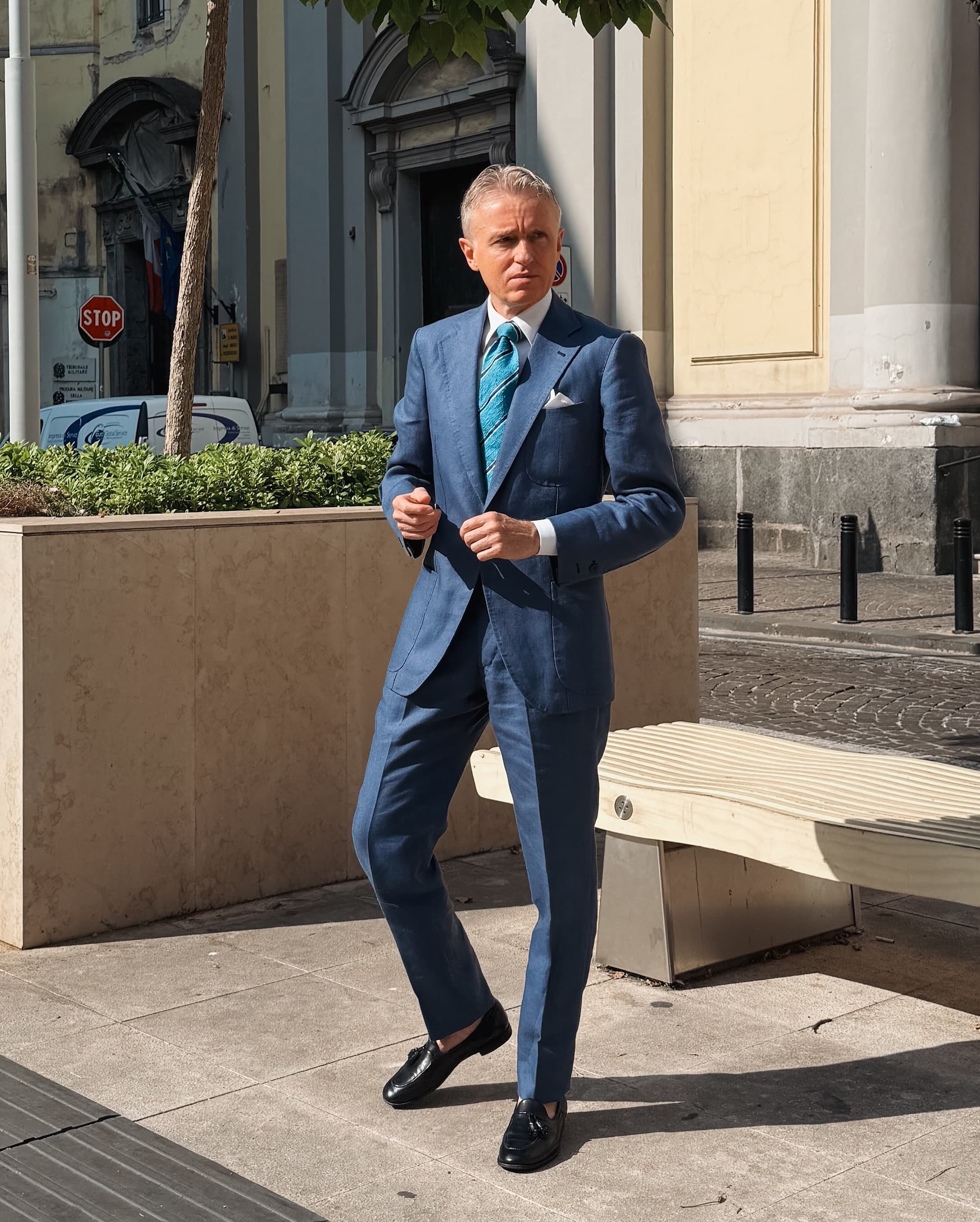 A man standing in Naples in a blue peak-lapel bespoke suit, white shirt and striped tie.