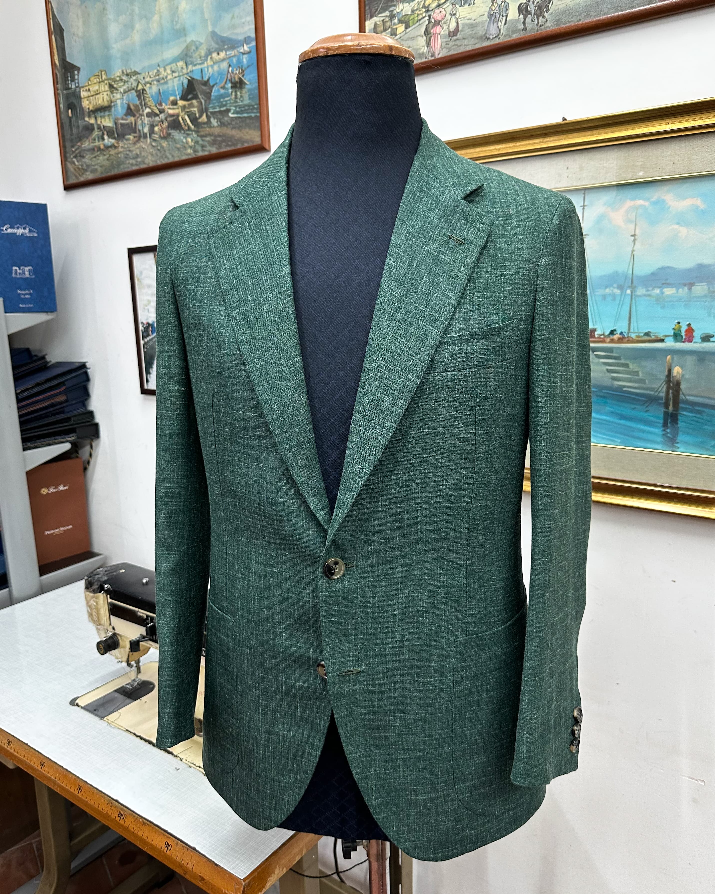 A forest-green textured tailored jacket with patch pockets, displayed on a tailor’s form.