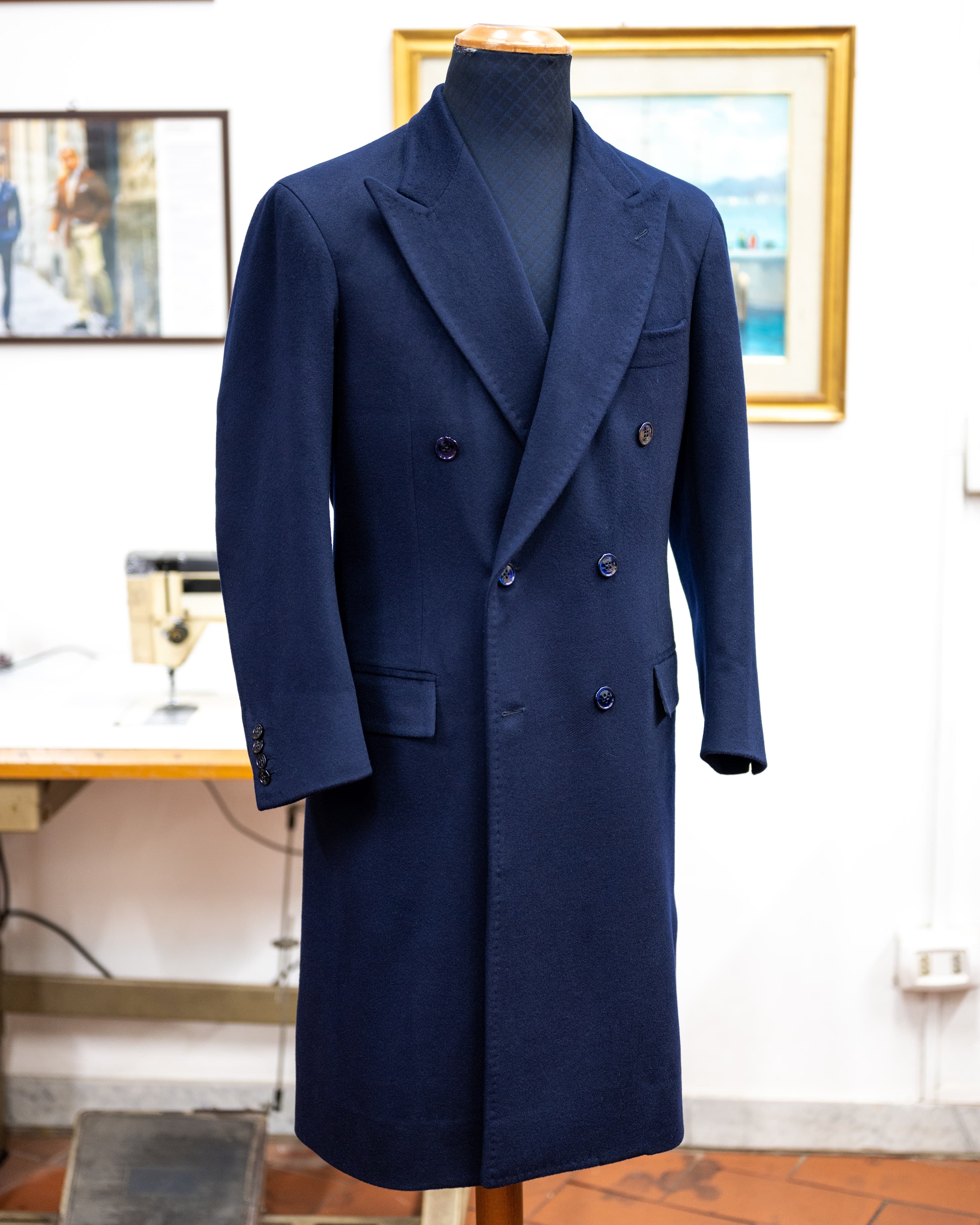 A navy double-breasted bespoke overcoat with peak lapels, displayed in the Naples atelier.