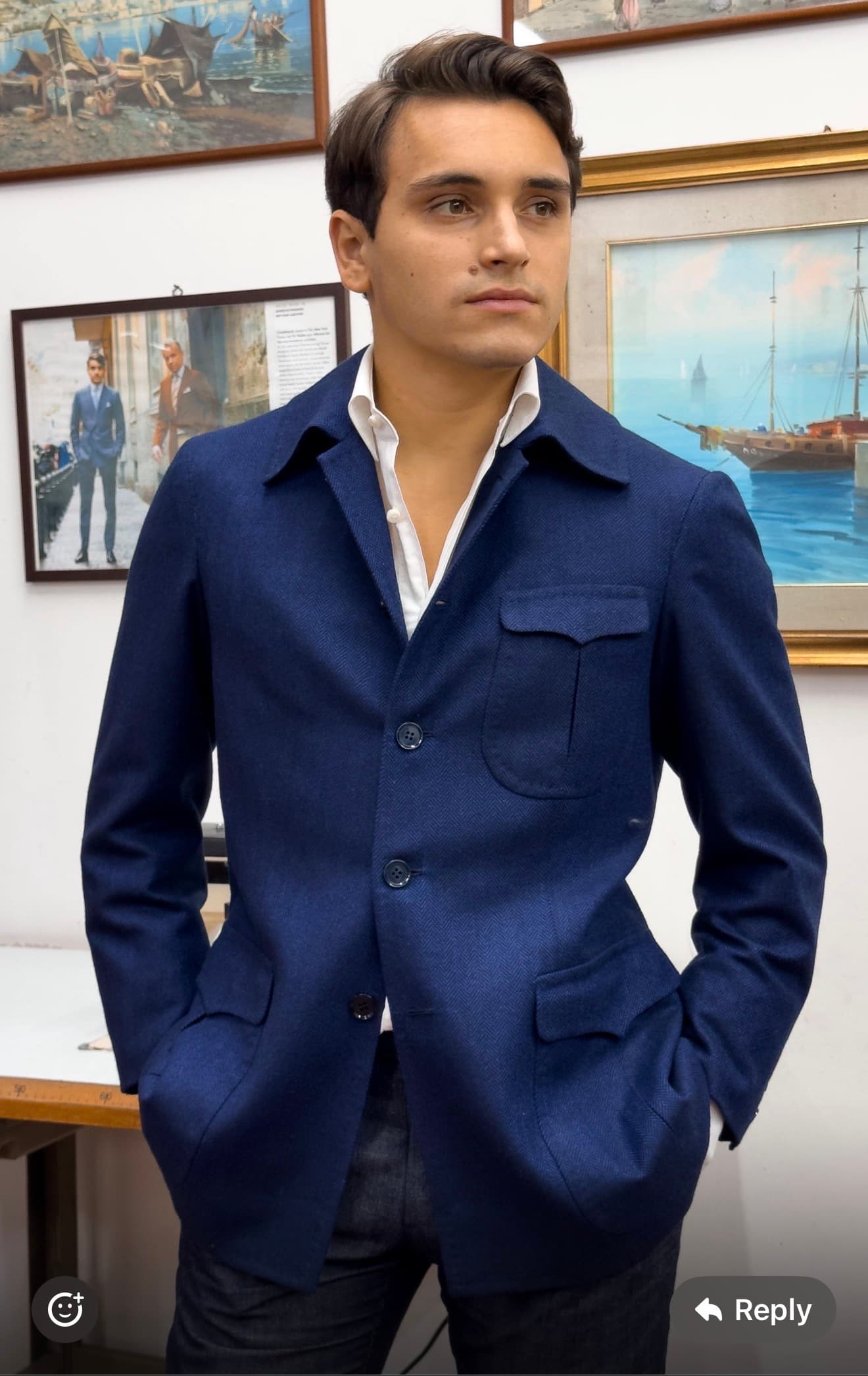 A man wearing a navy safari jacket with flap pockets and an open white shirt in the atelier.