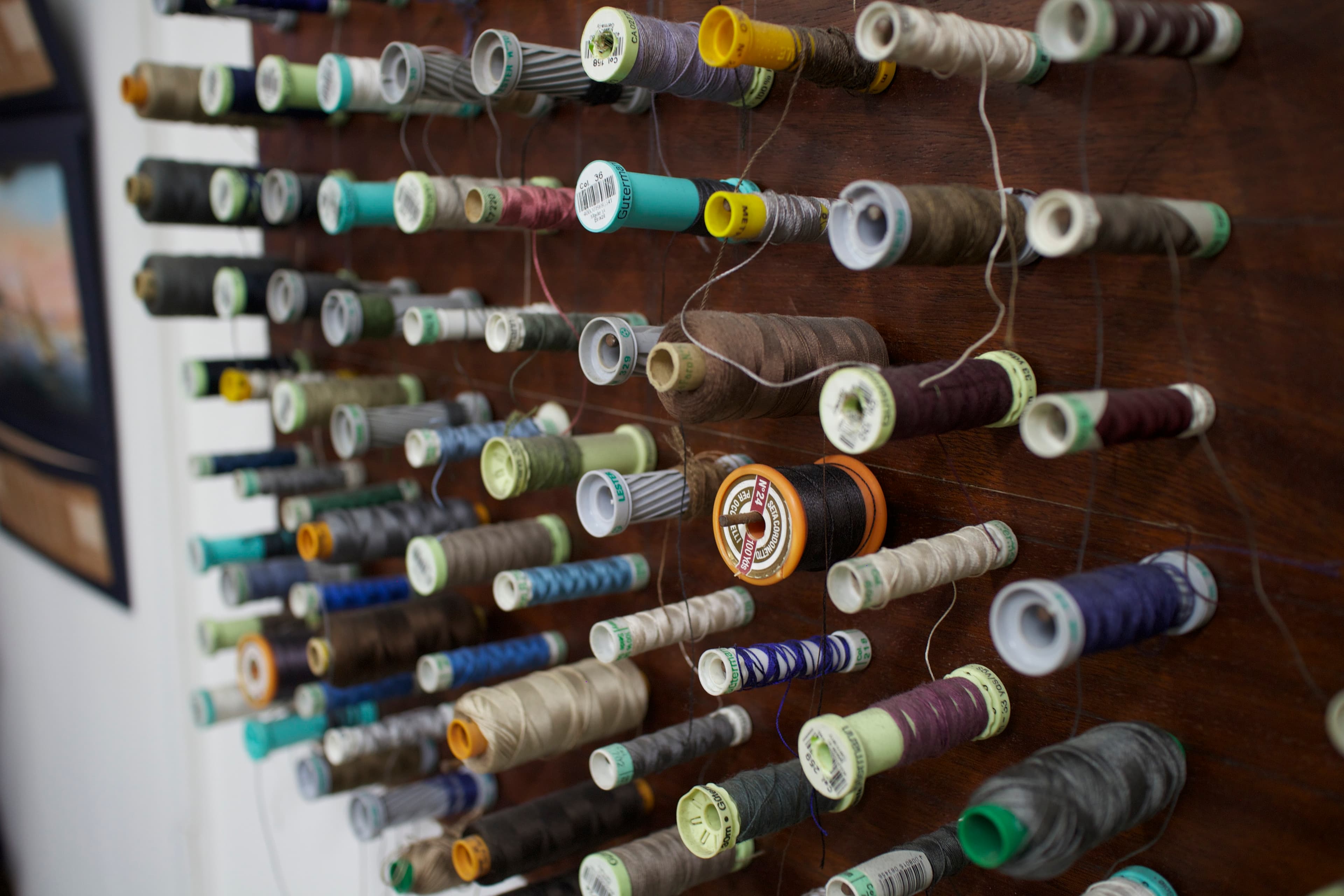 A wooden rack of sewing threads in many colours, some partly unwound.