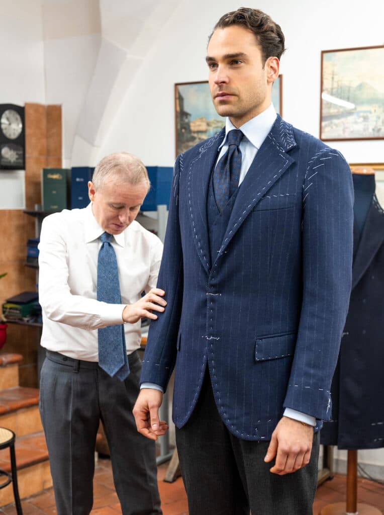 A tailor adjusting a navy jacket in white basting on a client during a fitting.